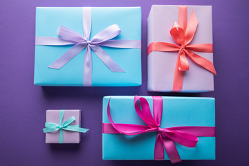 top view of colorful gift boxes with ribbons and bows on purple background