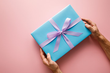 cropped view of man holding blue gift box with violet satin ribbon on pink background
