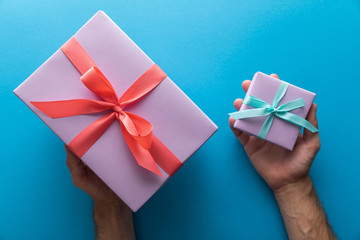 cropped view of man holding violet gift boxes with ribbons on blue background