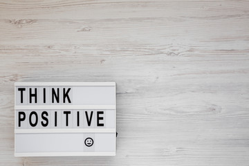 'Think positive' words on a lightbox on a white wooden surface, top view. Overhead, from above, flat lay. Space for text.