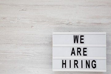 'We are hiring' words on a modern board on a white wooden background, overhead view. Top view, from above, flat lay. Copy space.