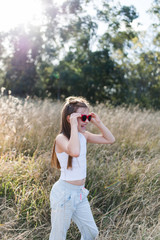 Young girl laughing with a big smile wearing red sunglasses. The girl has long brown hair and is standing in a field of long grass. The grass heads are glowing from the sun.