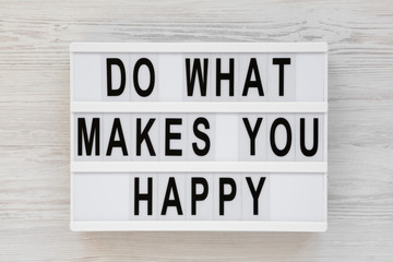 'Do what makes you happy' words on a lightbox on a white wooden surface, top view. Overhead, from above, flat lay.