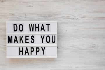 'Do what makes you happy' words on a modern board on a white wooden background, top view. Overhead, from above, flat lay. Copy space.