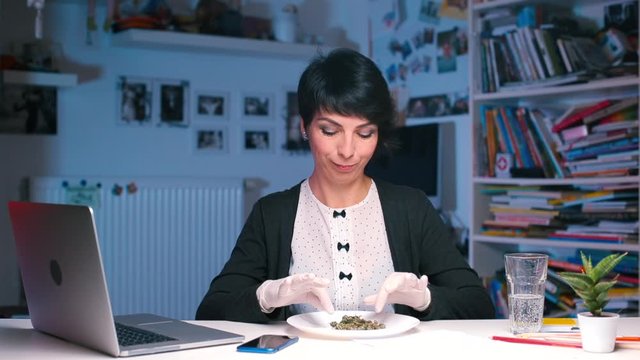 A girl sitting at a table in an office picks up a smartphone and takes photos of cannabis
