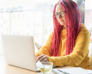 A woman is looking at laptop and is typing on keyboard. Girl with long pink hair, designer,...