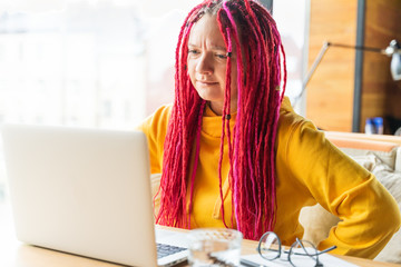Woman looks at laptop and gets angry, surprised, annoyed. Girl with long pink hair, designer,...