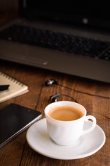 Cup of coffee on a laptop keyboard. Work place modern. Laptop (notebook) with cup of coffee and notepad with pen on old wooden table.