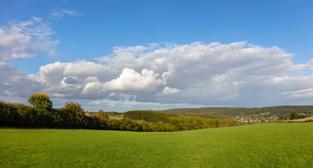 A landscape panorama with sunshine and beautiful clouds in the middle of Germany. In the distance you can see the small village Veldrom and in the background a forest.