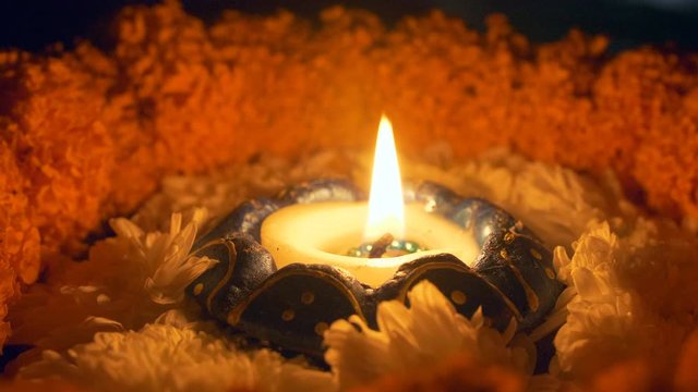Closeup shot of a burning oil lamp on a floral platform decorated for Diwali - Indian festival. Shot of beautiful flower garlands decorated around a colorful Diya radiating light in the dark on Diw...
