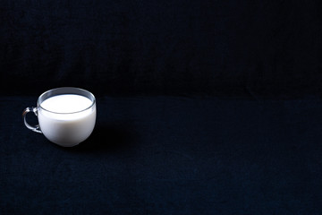 Glass mug with milk on dark fabric background