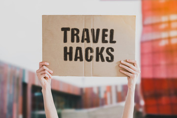 The phrase " Travel Hacks " drawn on a carton banner in men's hand. Human holds a cardboard with an inscription. Traveling. Traveler. Exploring © AndriiKoval