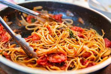A pan of rustic cooked spaghetti / pasta, sweet tomato sauce and basil leaves.