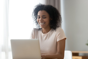Smiling biracial woman laughing using laptop messaging
