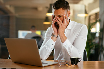 Tired businessman working on laptop in office