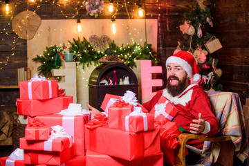 Obraz na płótnie Canvas Winter holidays. Cozy home atmosphere. Parcels gifts will be delivered to its destination. Sending gifts. Bearded man sit in armchair with pile of gifts. Greetings from Santa. Santa claus residence