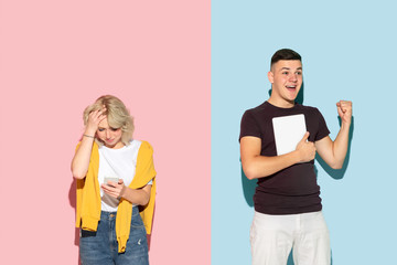 Young emotional man and woman in bright casual clothes posing on pink and blue background. Concept of human emotions, facial expession, relations, ad. Woman's sad, man's astonished, crazy happy.
