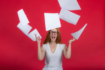 Portrait of a young attractive woman in glasses, throws a stack of documents up on a red background.