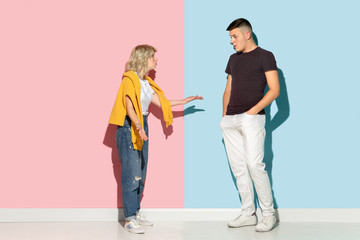 Young emotional man and woman in bright casual clothes posing on pink and blue background. Concept of human emotions, facial expession, relations, ad. Beautiful caucasian couple discussing angry.