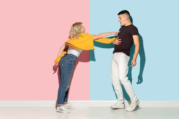 Young emotional man and woman in bright casual clothes posing on pink and blue background. Concept of human emotions, facial expession, relations, ad. Beautiful caucasian couple discussing angry.