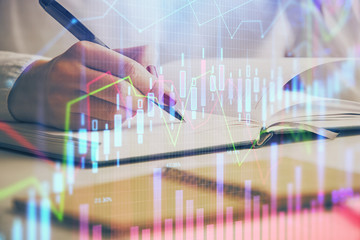 Double exposure of woman's hands making notes with forex graph hologram. Concept stock market analysis.