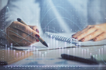 Double exposure of woman's hands making notes with forex graph hologram. Concept stock market...