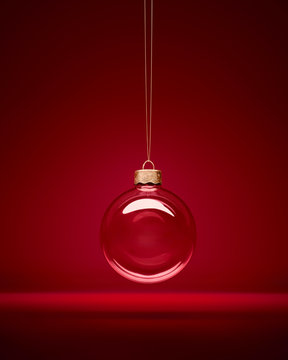 Christmas glass bauble hanging in front of luxury dark red background. Transparent winter decoration.
