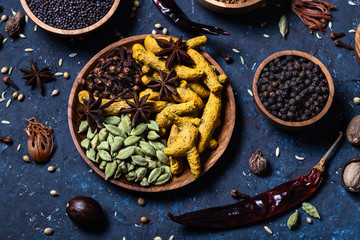 Dry whole warming Indian spices in wooden bowls on dark blue concrete background.
