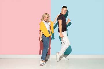 Obraz premium Young emotional man and woman in bright casual clothes posing on pink and blue background. Concept of human emotions, facial expession, relations, ad. Beautiful caucasian couple dancing together.