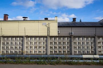 Old gray concrete fence with square relief pattern and razor wire at the top, gas pipeline in the...