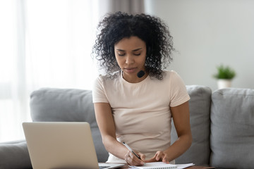 Focused black woman in headset studying on laptop at home