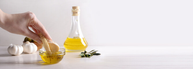 Woman dipping fresh bread into tasty olive oil on table with space for text