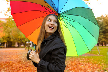 Cheerful young woman with colorful umbrella smiling back. Girl in park with raincoat and umbrella in the autumn.