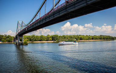 Fototapeta premium Tour of Kiev in the center of Europe. View of the Dnieper, Trukhanov island and a foot bridge. Park fountain and sunset on the horizon..
