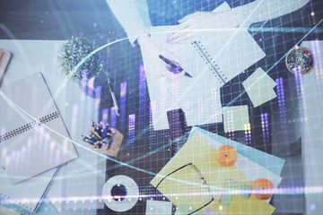 Hand taking notes in notepad. Forex chart holograms in front. Concept of research. Double exposure