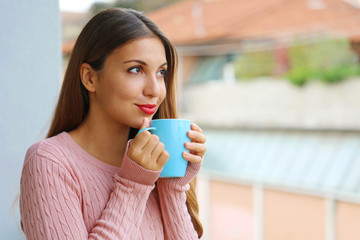 Close up of young woman with warm sweater enjoying hot drink in the morning at home on balcony outdoors.