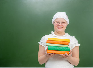 Smiling girl with Down Syndrome stands near a school board with books. Empty space for text