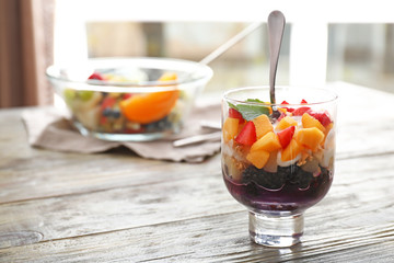 Glass of tasty fruit salad on wooden table