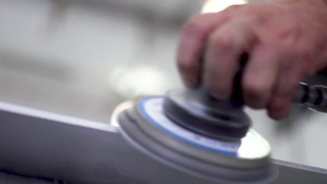 Close up of a worker firmly holding a small sanding machine to smooth out the sides of a metal sheet. Slow motion.