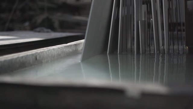 Metal rack full of steel sheets are being dipped slowly in a tub that contains a chemical solution. Metal workshop. Slow motion. 