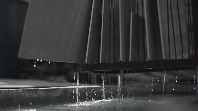 Metal sheets coming out of a rinsing tub. Water dripping from the rack. Beautiful water drops falling down into the tub. Metal factory. Slow motion.