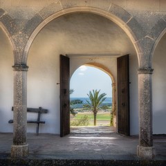 Fototapeta na wymiar Monastery of Montesión with ancient wooden doorway framed by Gothic pillars leading to a view of palm trees and hills, Porreres, Mallorca, Spain