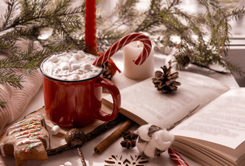 mug of hot chocolate with marshmallow and Lollipop by the window, candle, cookies, open book, cone, winter drink