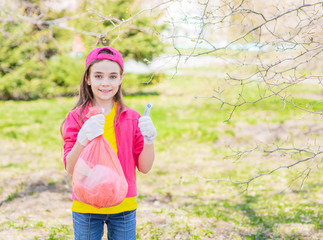 Girl with a bag of trash in a summer park showing thumbs up. Volunteer and ecology concept. Empty space for text