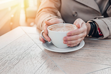 Big coffee white cup in woman's hands with pastel manicure while sitting in cafe.