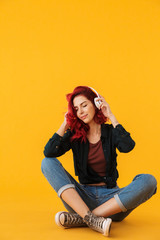 Image of pleased cute woman using headphones while sitting on floor
