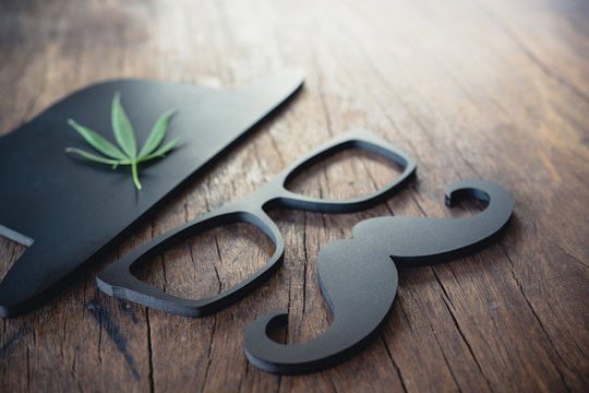 A masculine symbol, mustache, glasses and black hat with a hemp leaf beside it resting on an old wooden floor.