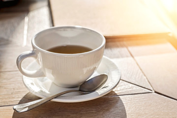 White big cup of black tea on wooden table in sunset light with copy space.