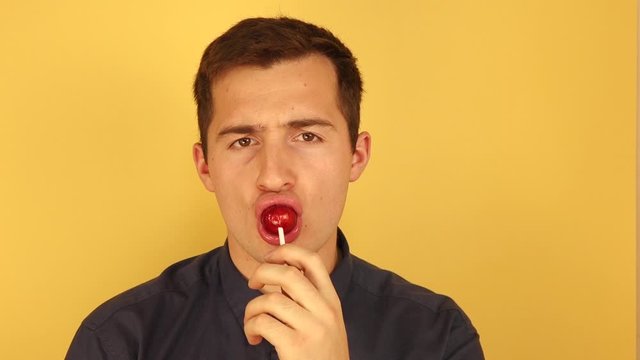 a man sucks a Lollipop standing on a solid orange background