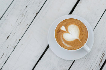 White big cup of delicious coffee with shaped heart art on white wooden table with copy space.
